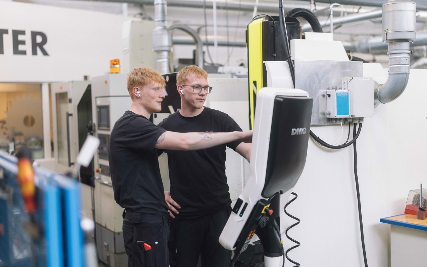 To unge mænd står og kigger på en skærm foran en stor maksine.