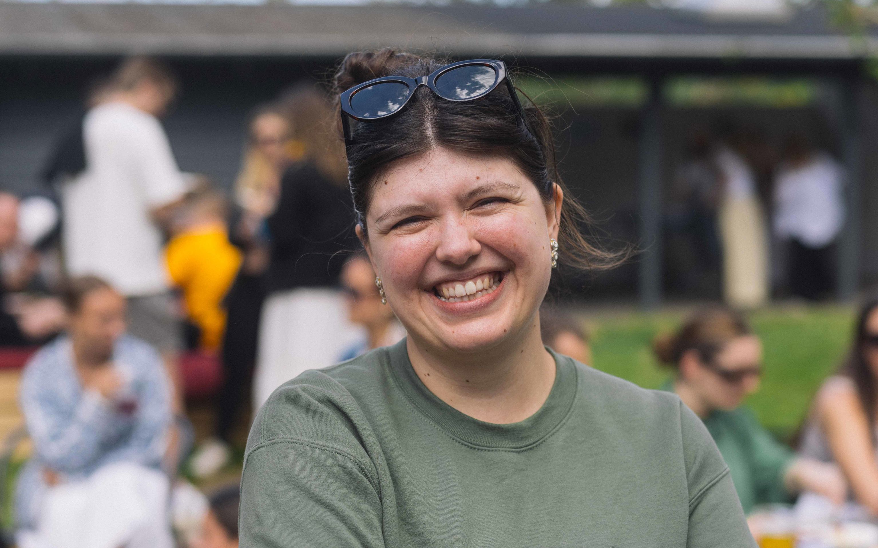 Ung kvinde smiler til kameraet. Hun har armene over kors solbriller i håret. På hendes sweatshirt står der "VEJLE".