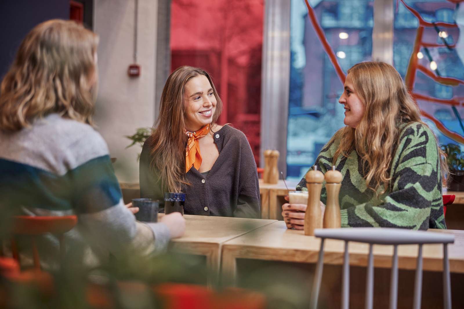 Tre unge kvinder sidder om et bord og snakker sammen.